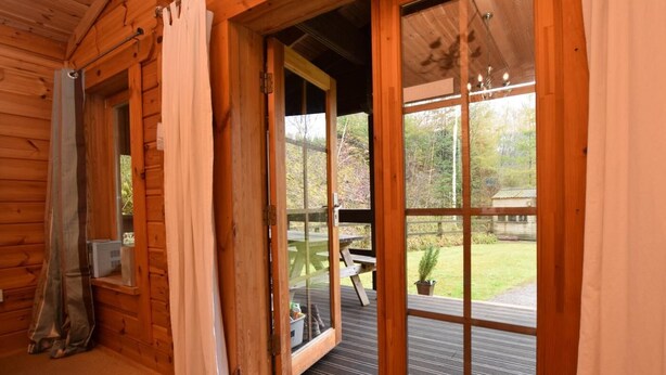 Una cabaña de madera con un gran ventanal corredera que da a un patio al aire libre con una mesa y sillas.