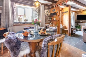 A cozy dining area with a round table, chairs with fur throws, a vase with flowers, and a stone wall. - 2 Bed in Liskeard (oc-04708) (Menheniot)