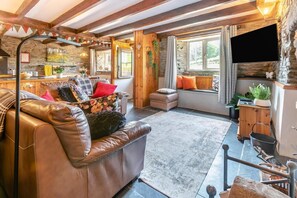 A cozy living room with a leather sofa, a stone fireplace, and a large window with curtains. - 2 Bed in Liskeard (oc-04708) (Menheniot)