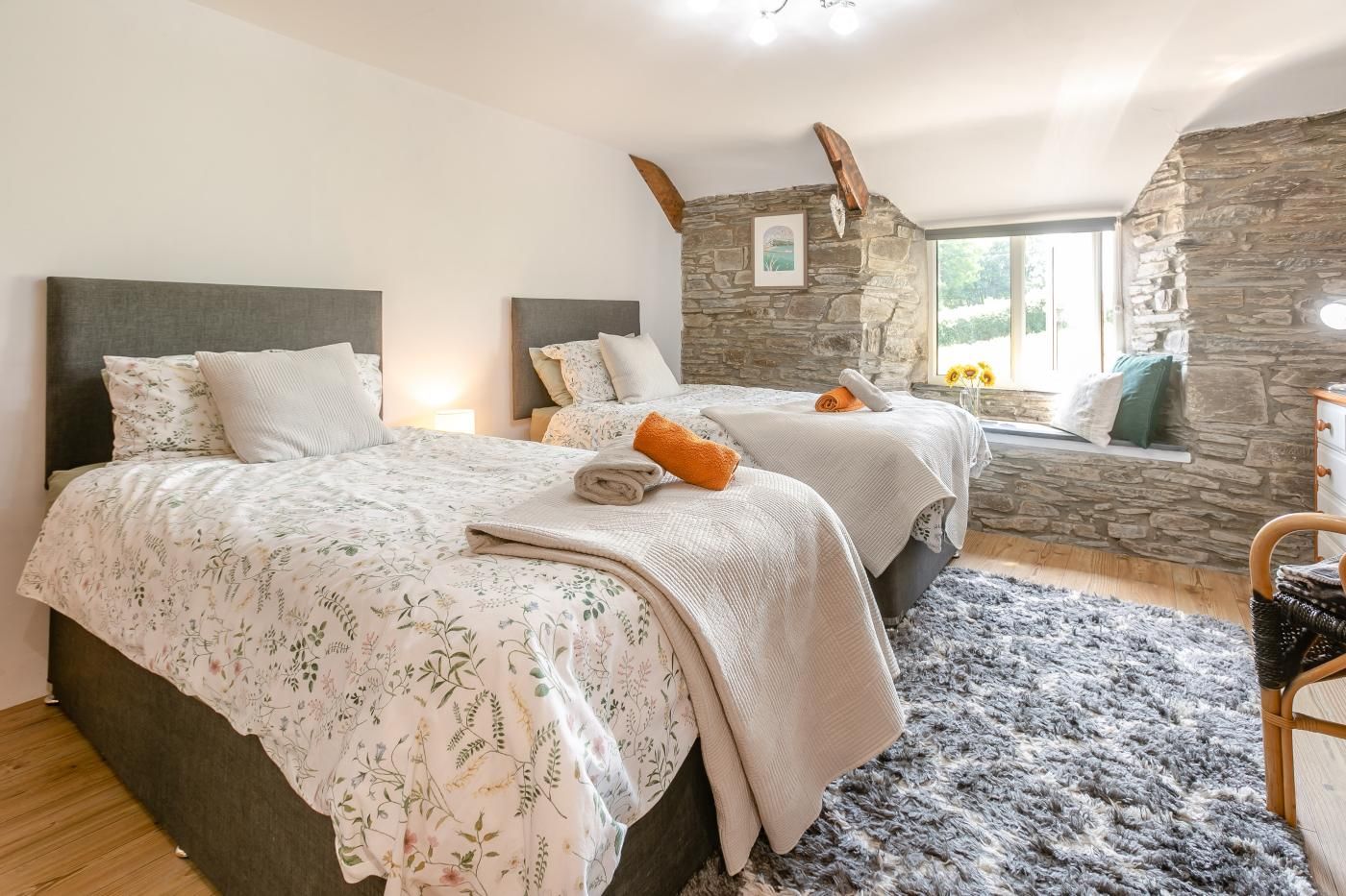 A bedroom with two beds, a stone wall, a window with a view, and a wooden floor.