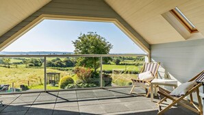 Ein Balkon mit Blick auf eine grüne Landschaft, ein Holzstuhl und ein kleiner Tisch.