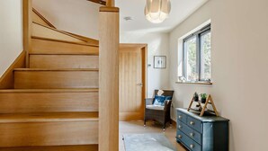 Eine Holztreppe führt zu einem Raum mit einem Korbstuhl, einem Schminktisch und einem Fenster.