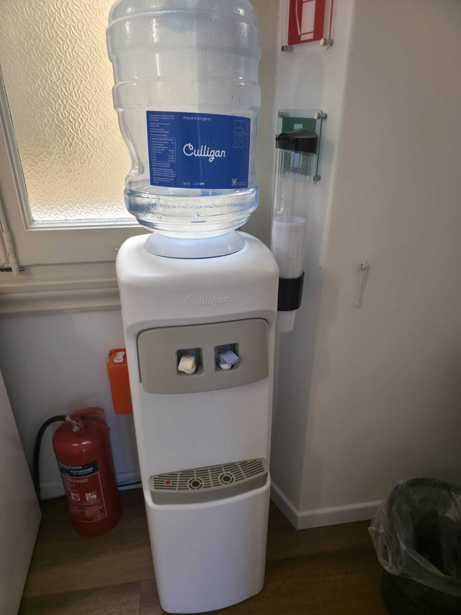 Un distributeur d’eau avec une grande bouteille d’eau placée sur le dessus, un extincteur et une poubelle.