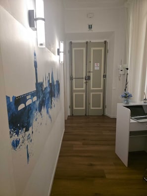 A hallway with a cityscape mural, double doors, a desk with a laptop, and a small vase of flowers. - Aura Suites Florence (Florence)