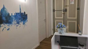 A hotel lobby with a wall mural, a reception desk, and a door with a 'No Smoking' sign.