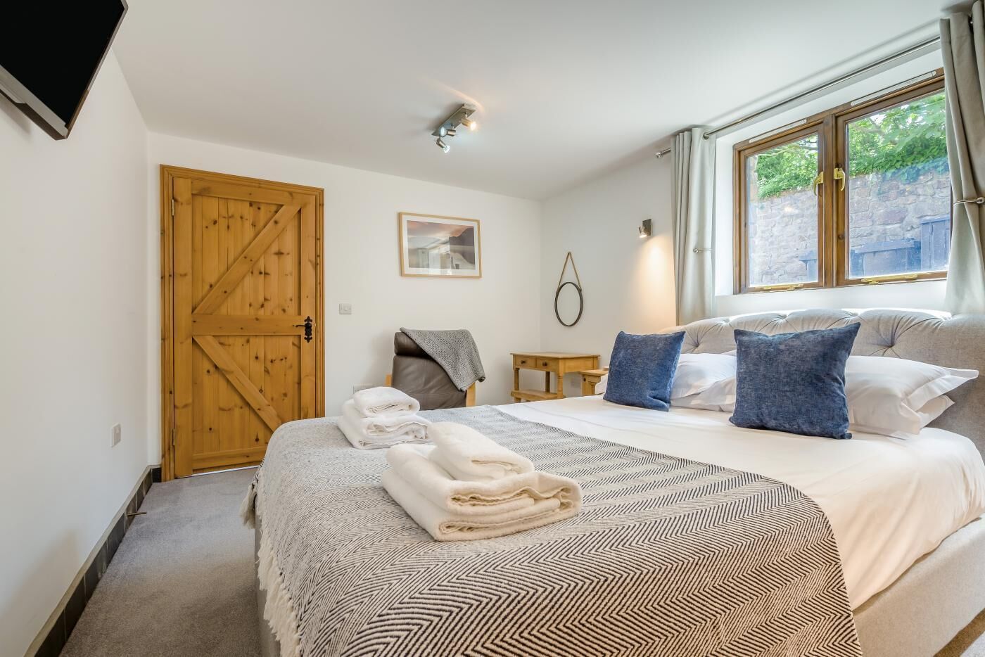 Une chambre à coucher avec un grand lit, une porte en bois, une petite table et une fenêtre avec des rideaux.