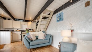 Ein gemütliches Zimmer mit einem blauen Sofa, einem kleinen Tisch mit einer Lampe und einer Küchenzeile im Hintergrund.
