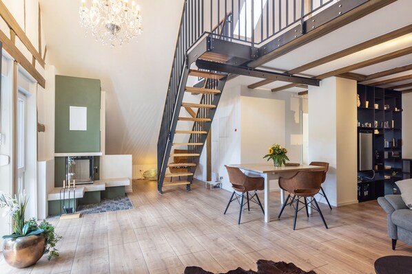 A modern interior with a wooden staircase, a dining area with chairs, and a chandelier.