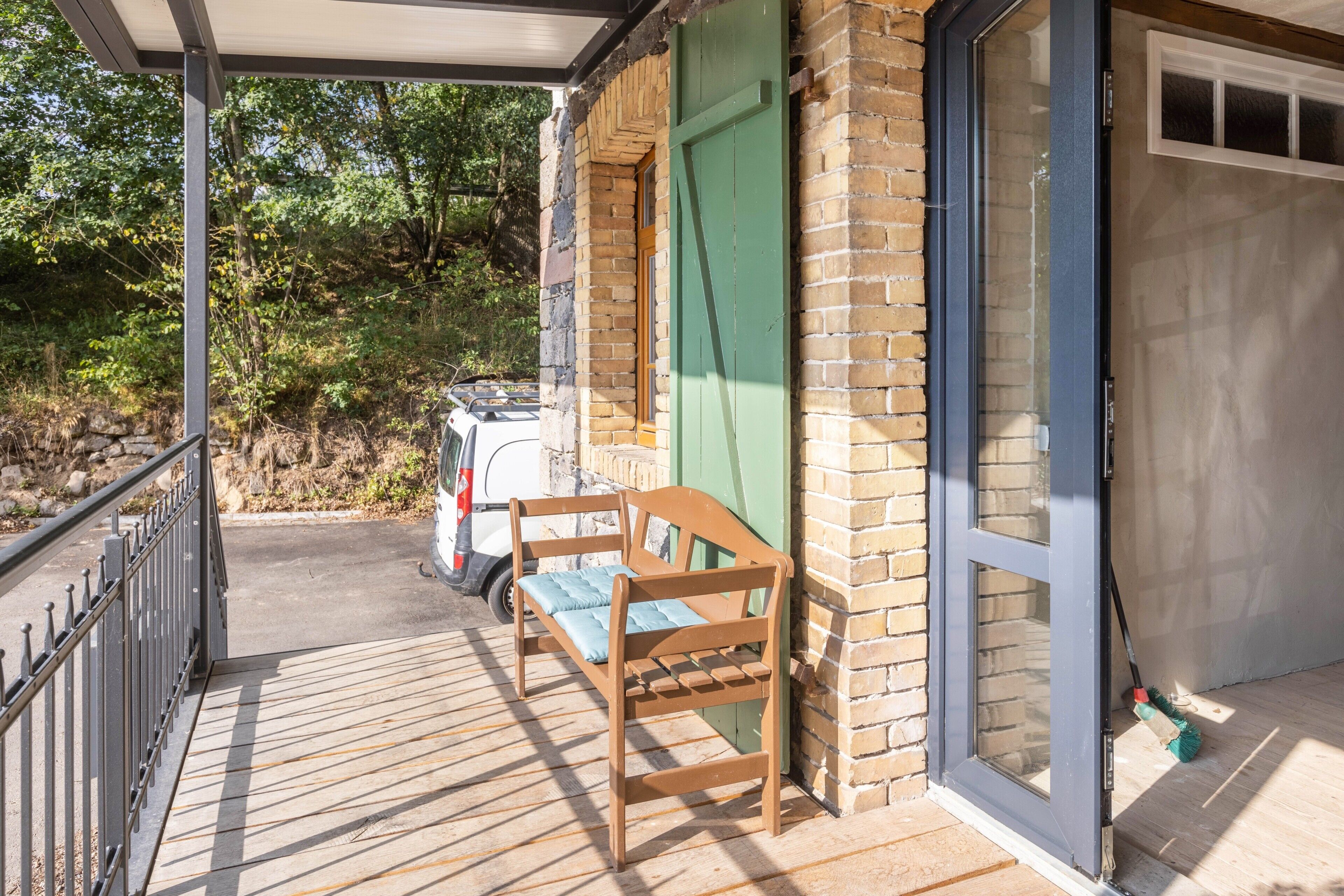A wooden bench on a balcony with a brick wall and a glass door.
