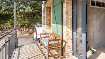 A wooden bench on a balcony with a brick wall and a glass door.
