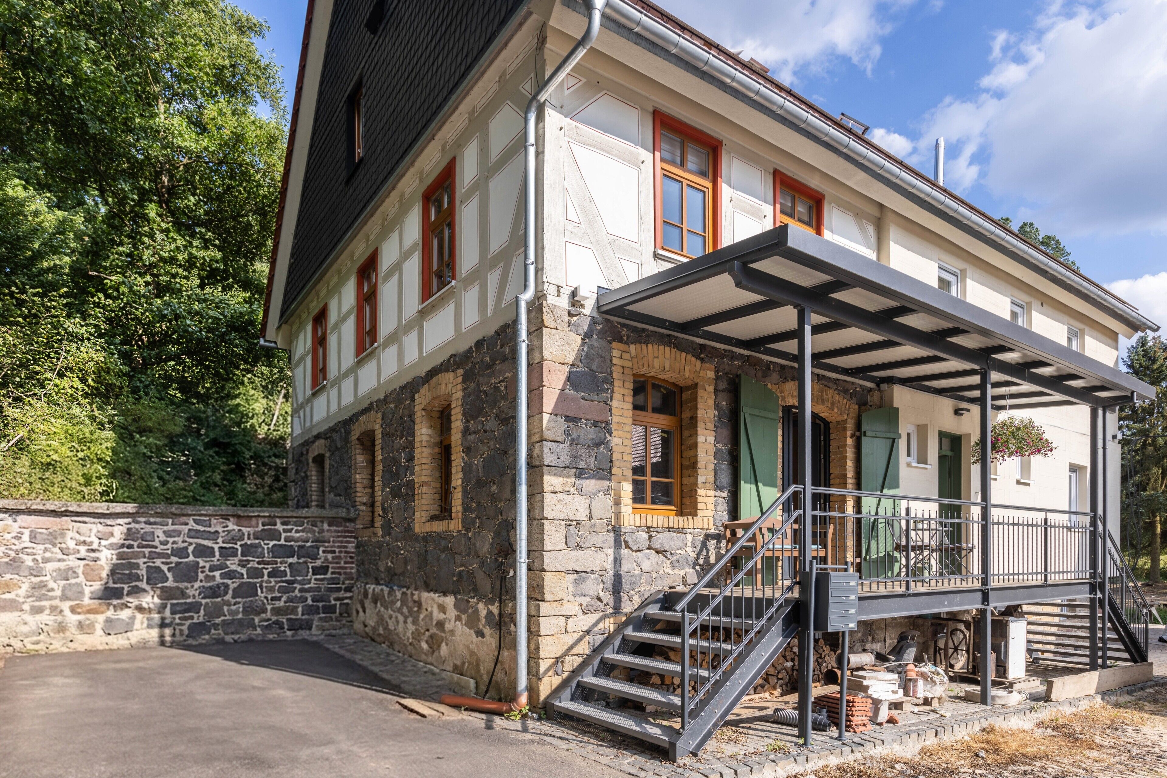 Un bâtiment à deux étages doté d’une façade en pierre, d’un porche couvert avec une rambarde en métal et d’un escalier menant à l’étage supérieur.