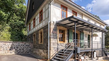Un bâtiment à deux étages doté d’une façade en pierre, d’un porche couvert avec une rambarde en métal et d’un escalier menant à l’étage supérieur.