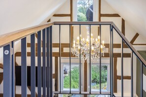 Una escalera con barandilla de madera y balaustradas de metal que lleva a una habitación con candelabro y vistas al exterior con vegetación.