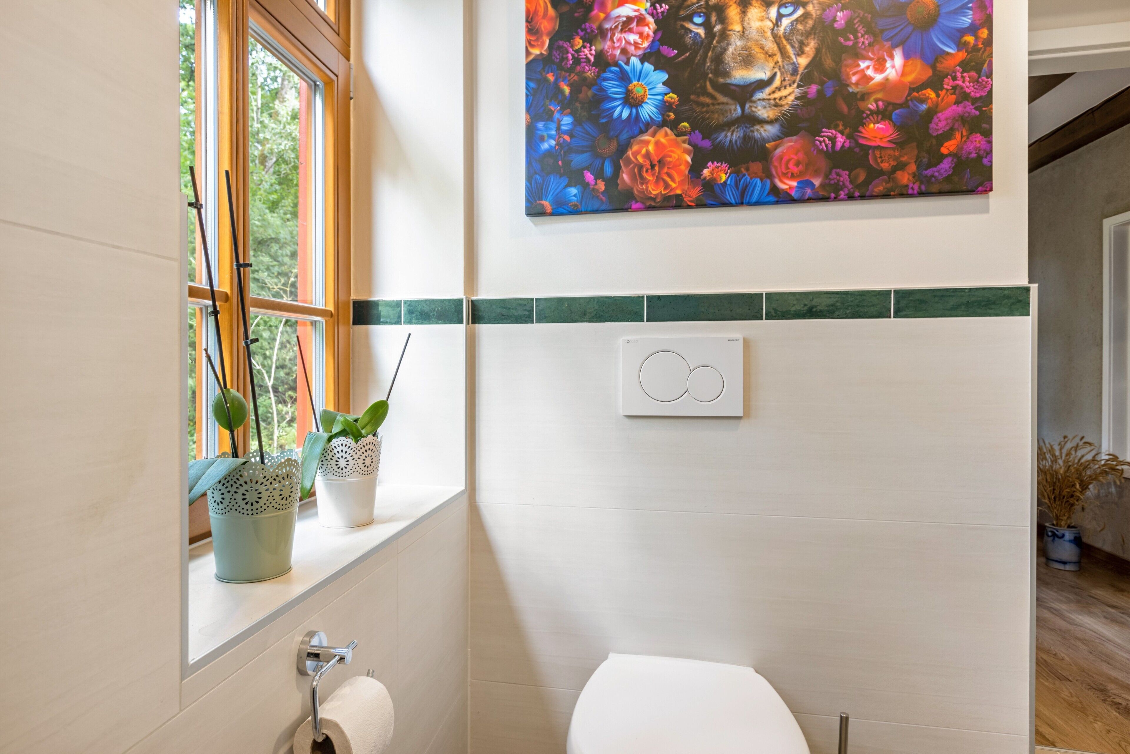 Une salle de bain avec des toilettes, une fenêtre ornée de plantes et un interrupteur fixé au mur.