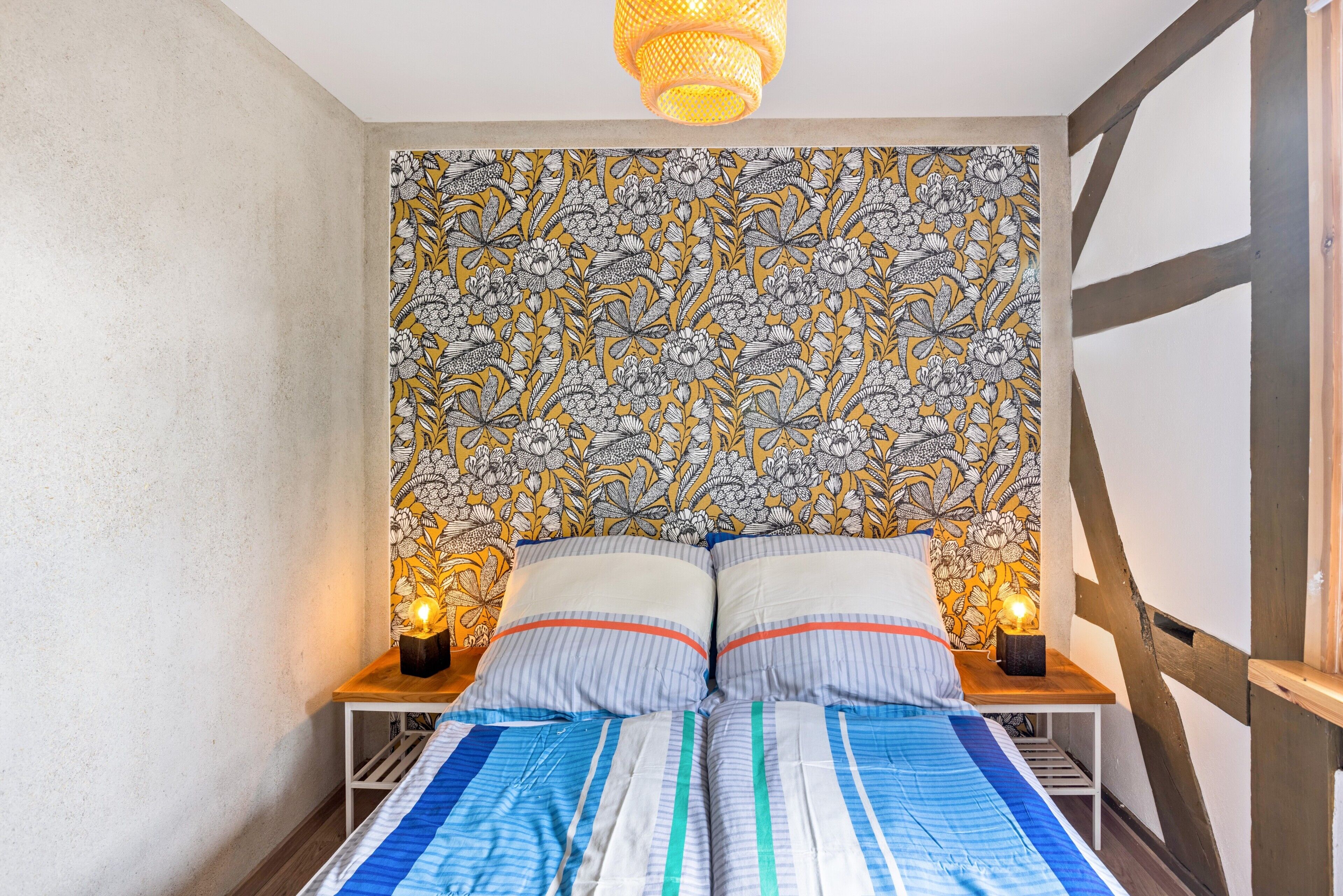 Ein Schlafzimmer mit einem Bett, zwei Nachttischen, einer gemusterten Tapete und einer Pendelleuchte.