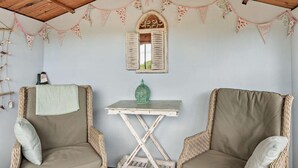 Een kamer met twee rieten stoelen, een bijzettafeltje, een decoratieve spiegel en een vlaggenlijn.