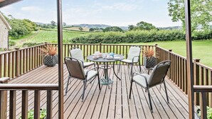 Een houten terras met een tafel en stoelen, met uitzicht op een groen landschap.