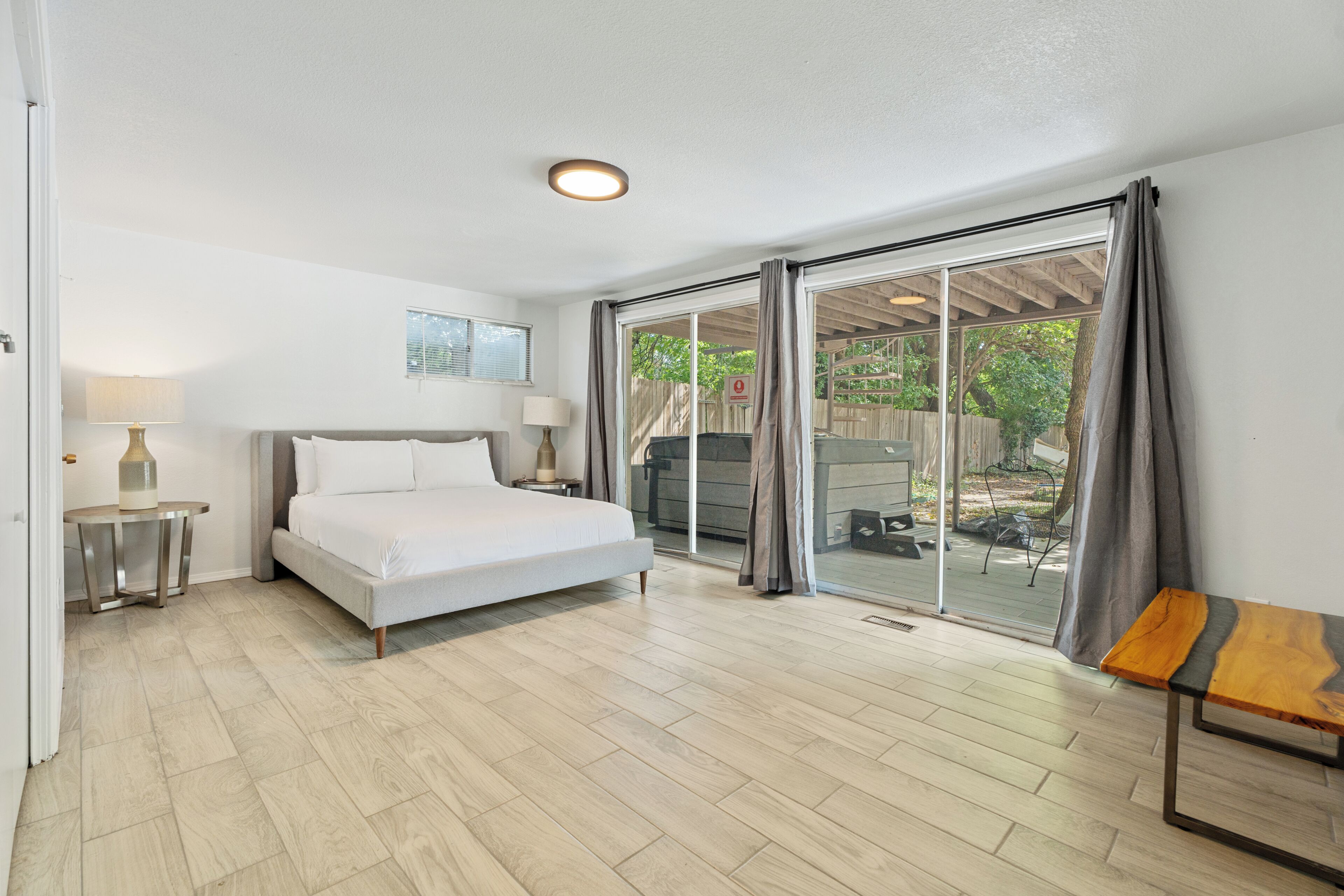 A bedroom with a bed, bedside tables, a lamp, and a view through a sliding glass door to an outdoor area.