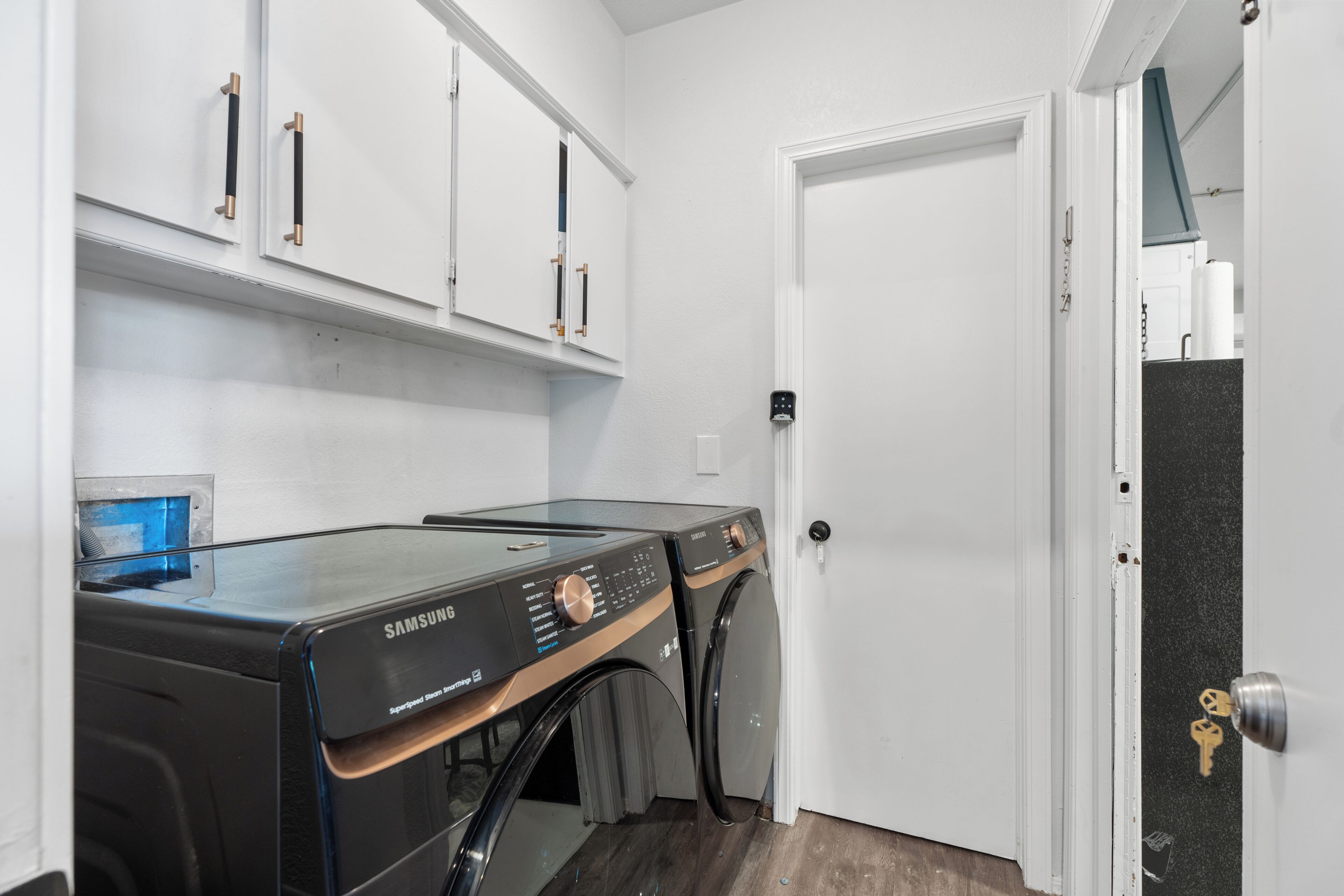 A laundry room with two Samsung washing machines, a white door, and a shelf above the machines.
