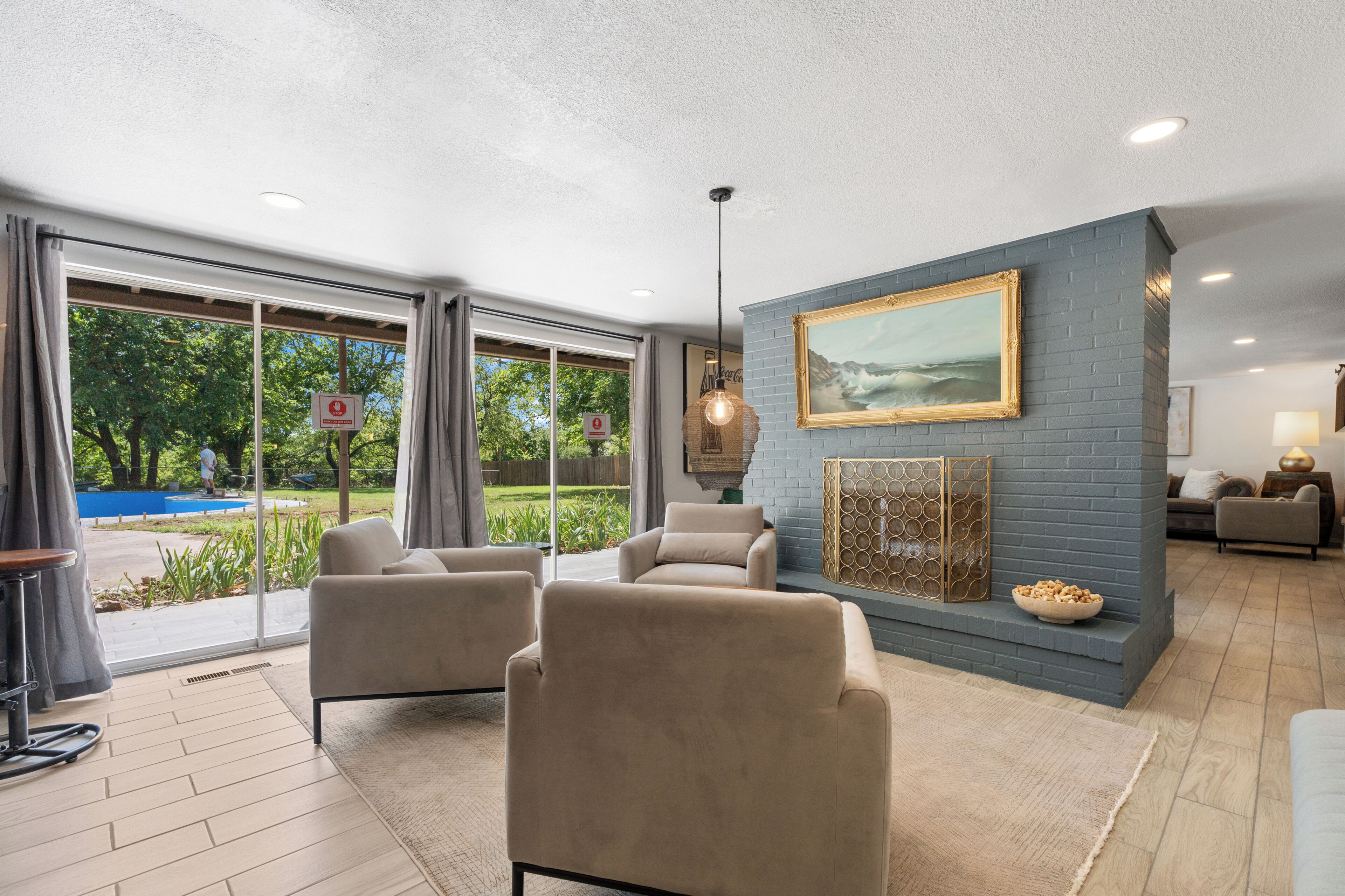 A spacious living area with a large window, a blue brick accent wall, and a painting.