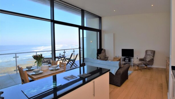 A modern kitchen with a large window overlooking the ocean, a dining area with a table and chairs, and a seating area with a sofa and armchairs. - 2 Bed in Bideford (oc-tcseren) (Westward Ho!)
