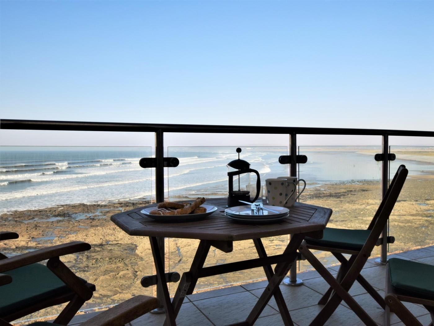Ein Balkon mit Tisch für zwei Personen, mit Blick auf einen Strand und Wellen.