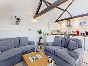A modern living room with two grey sofas, a wooden coffee table with a magazine, and a kitchen in the background. - 1 Bed in Dulverton (oc-lbard) (Dulverton)
