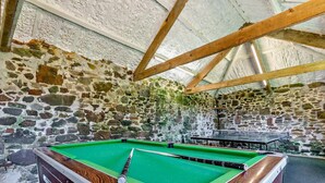 Una mesa de billar en una sala con paredes de piedra y vigas de madera.