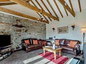 A living room with stone walls, wooden beams, leather sofas, a TV, and a fireplace. - 3 Bed in Bude (oc-woodu) (Poundstock)