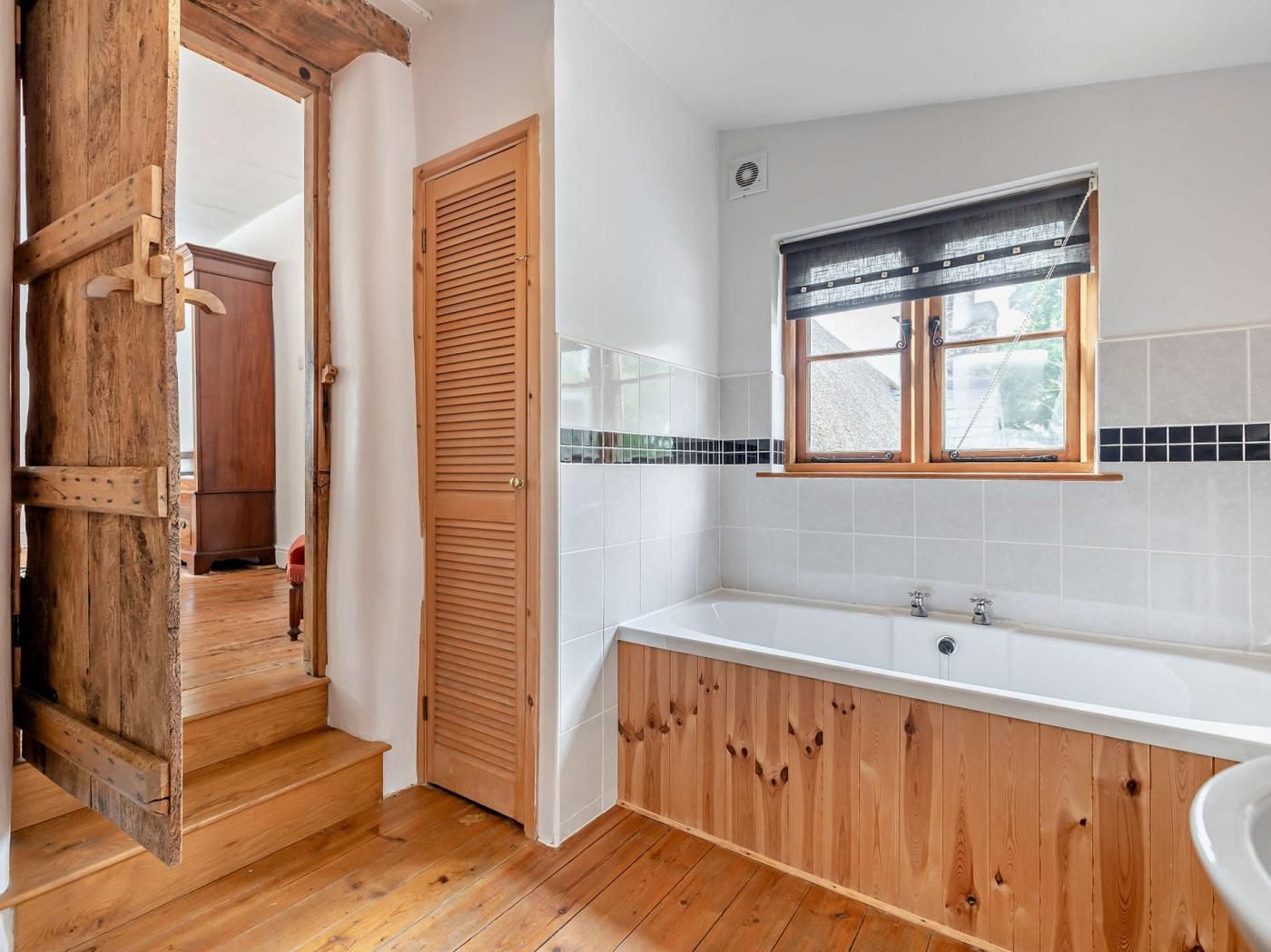 A bathroom with a wooden vanity, a bathtub, and a window with blinds.