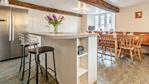 A kitchen with a wooden ceiling, white cabinets, a central island with stools, and a dining area with wooden chairs and a table. - 6 Bed in Winkleigh (oc-furfa) (Iddesleigh)