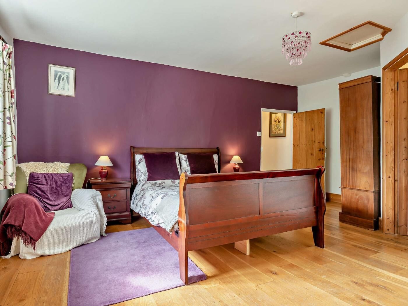 Une chambre à coucher avec un lit en bois, une table de chevet, une chaise, un tapis violet et une armoire en bois.