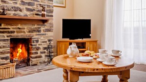 Ein gemütliches Zimmer mit einem Steinofen, einem Fernseher auf einem Holzboden und einem runden Holztisch mit Tellern, Tassen und einem Teekessel.