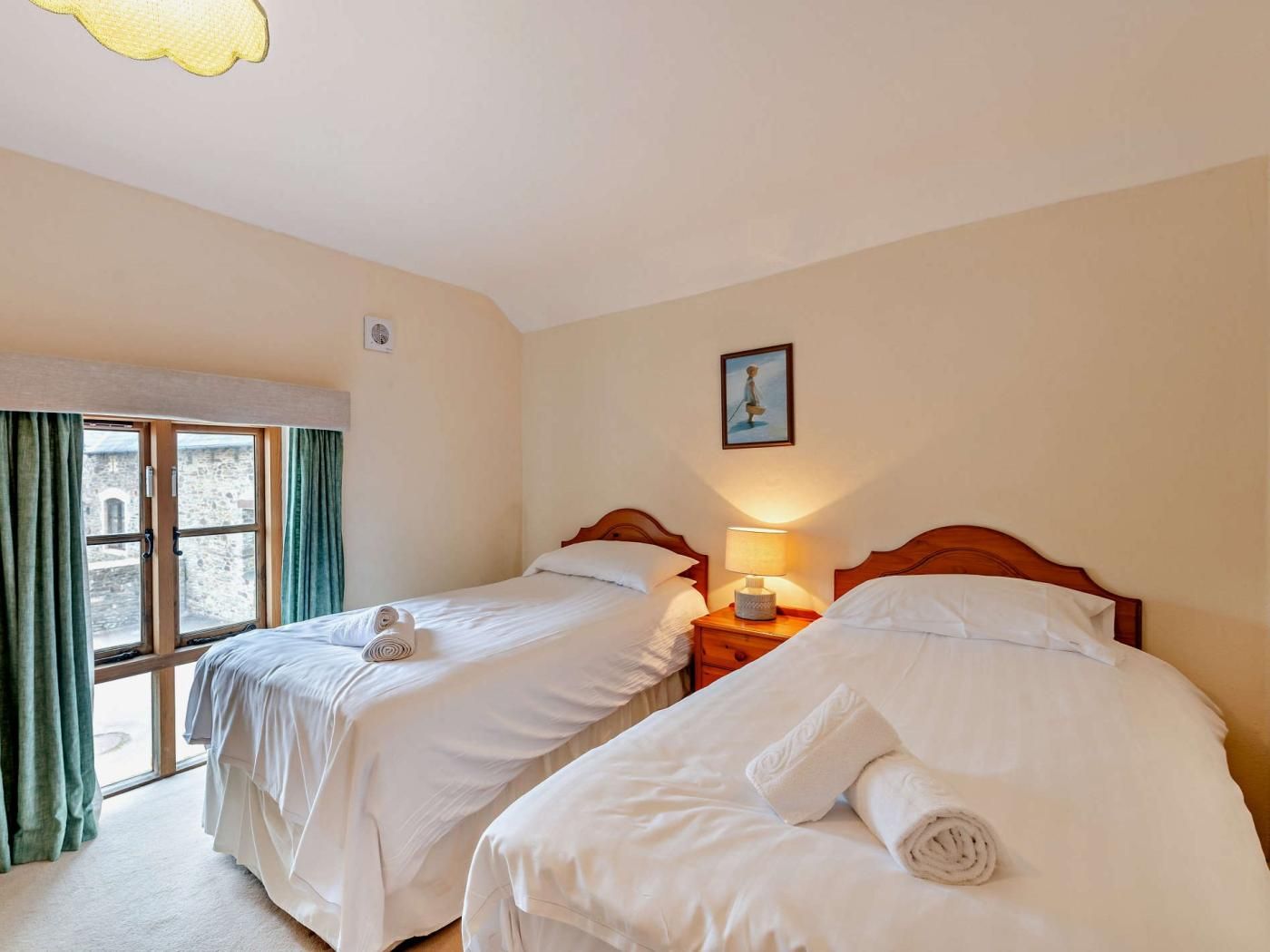 Habitación de hotel con dos camas individuales, una ventana con cortinas, una lámpara de noche y un cuadro en la pared.