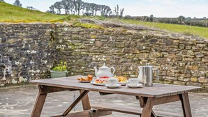 A picnic table with a stone wall backdrop, a clear sky, and a grassy hill in the distance. - 3 Bed in Plymouth (oc-combv) (Wembury)