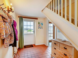 Ein Zimmer mit einer Holztreppe, einer Tür mit Blick, einem Schminktisch und einem an der Wand befestigten Kleiderhaken mit Jacken.