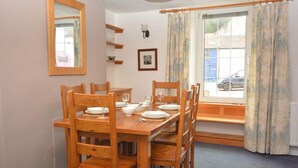 Un comedor con una mesa y sillas de madera, una ventana con cortinas, un espejo en la pared y un cuadro enmarcado.