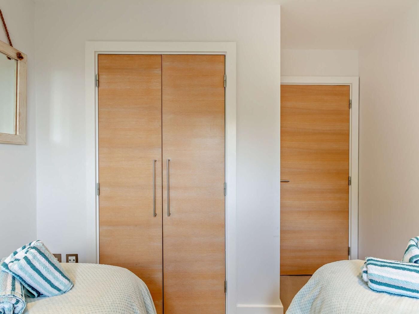 A room with two beds, a wooden wardrobe, and a mirror on the wall.