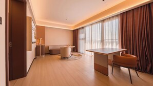 Habitación de hotel moderna con piso de madera, una mesa redonda, un sofá y un ventanal con cortinas.