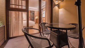 Un área de estar al aire libre techada con sillas de mimbre y una mesa redonda, contigua a una habitación con cama y mesita de noche.
