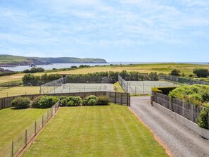 A tennis court surrounded by a fence, with a view of the sea and hills in the background. - 2 Bed in Kingsbridge (oc-wdelv) (Thurlestone Sands)