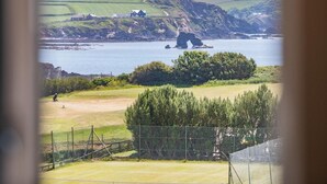 Un paisaje costero con un campo de golf, un promontorio rocoso y casas a lo lejos.