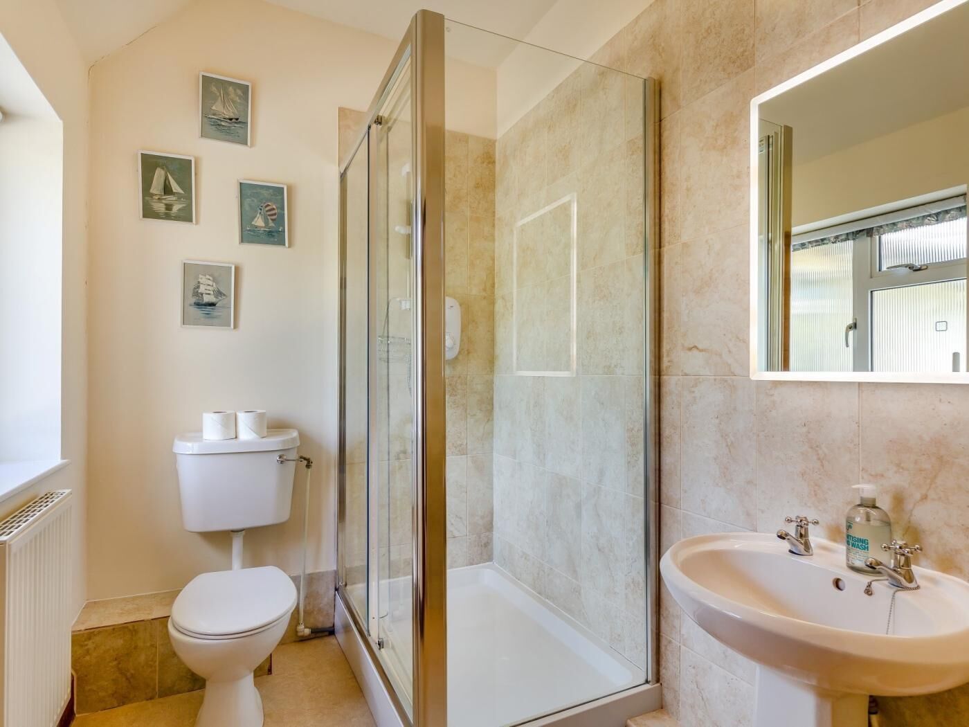 Et badeværelse med en brusekabine i glas, et toilet og en vask med et spejl over.