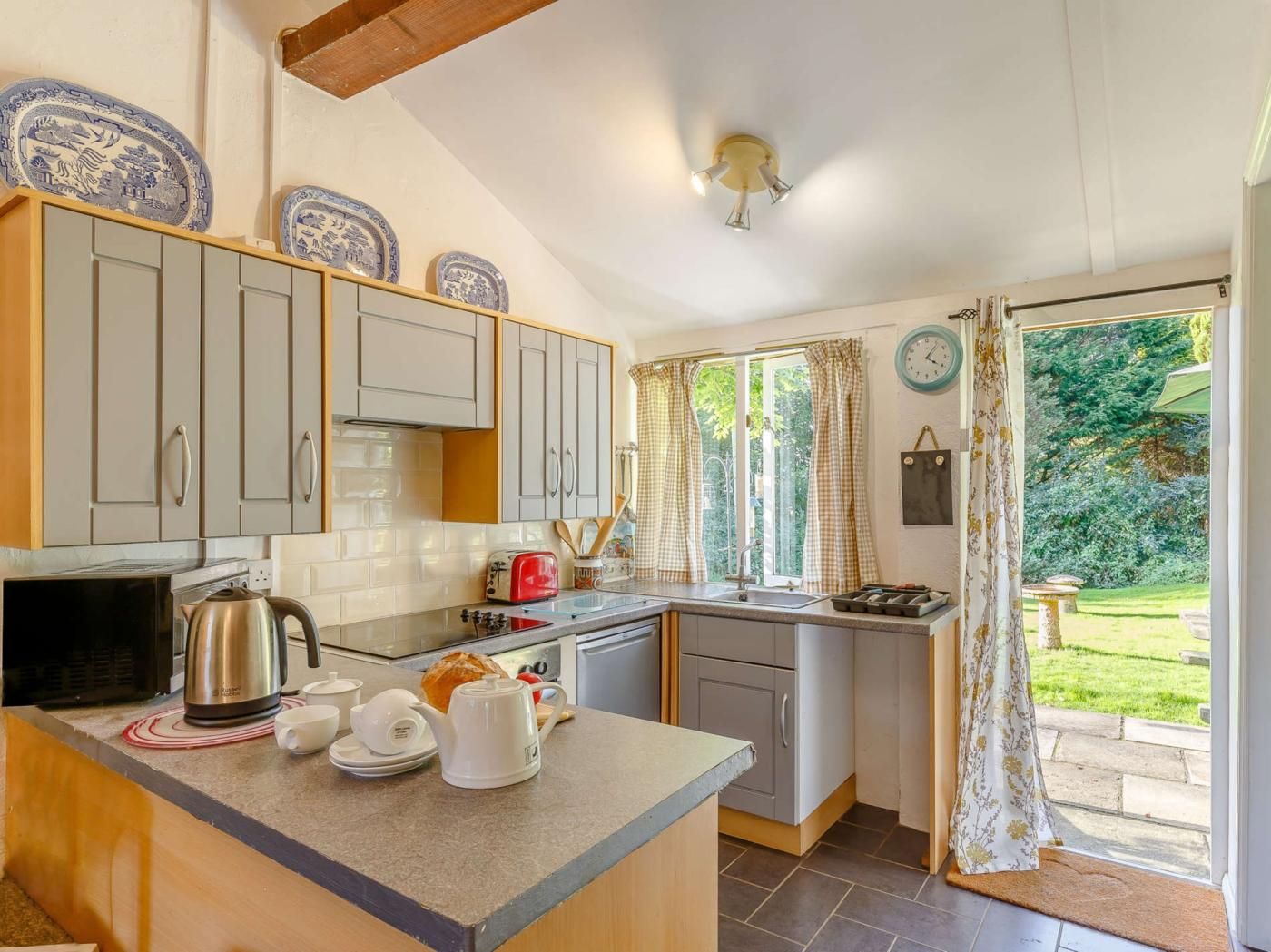 A kitchen with a microwave, kettle, toaster, and a small island with cups and a teapot.