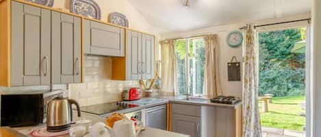 A kitchen with a microwave, kettle, toaster, and a small island with cups and a teapot.
