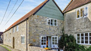 A stone building with a green roof, a stone wall, and a small table with flowers. - 1 Bed in Yeovil (oc-poloc) (West Camel)