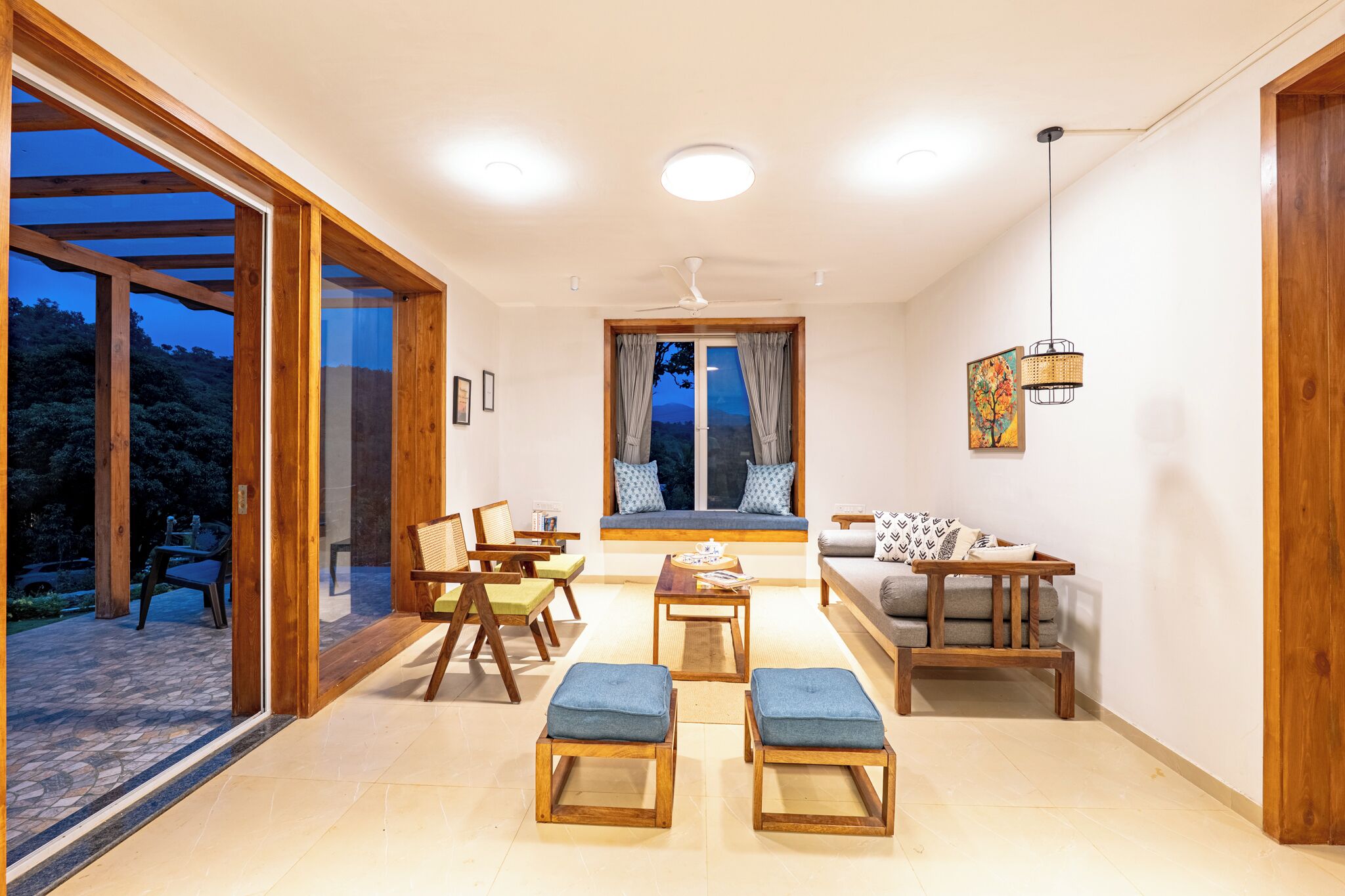 Un salon moderne comprenant un canapé, une table basse et des poufs, un coin repas avec des chaises, et une grande porte-fenêtre coulissante donnant sur une terrasse extérieure.