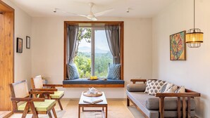A room with a large window, wooden furniture, a ceiling fan, and a wall-mounted light fixture. - CosmicStays Yutori  (Mulshi)