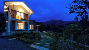 A modern two-story house with a well-lit entrance, a stone pathway, and a mountainous backdrop. - CosmicStays Yutori  (Mulshi)