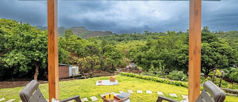 A covered outdoor seating area with a view of a lush garden and distant hills.